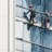 Two workers wearing safety gear are suspended by ropes on the side of a glass building, cleaning the windows. They are equipped with buckets and tools as they perform their task at significant heights.
