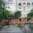 A group of workers wearing orange safety uniforms and helmets are cleaning a paved street area near a crosswalk. They are using hoses and brooms to clean the wet surface. Surrounding buildings, including a hotel named 'ROYAL HOTEL SAIGON,' and trees can be seen in the background.